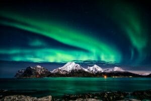 "Vibrant aurora borealis lights up the night sky above the snowy peaks of the Lofoten Islands, creating a breathtaking view."