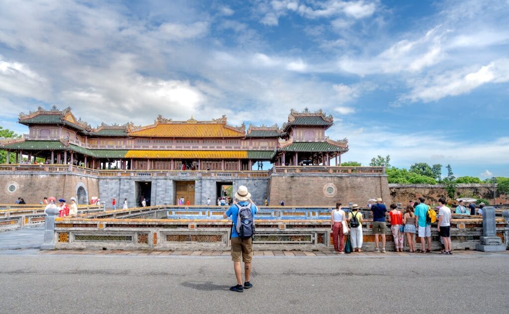 Tourists gather at the Imperial City of Hue, showcasing traditional Vietnamese architecture under a blue sky.