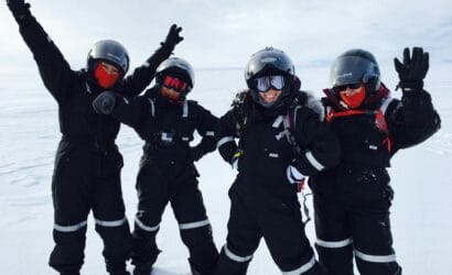 Four adults in winter suits and helmets enjoying a snowy adventure.