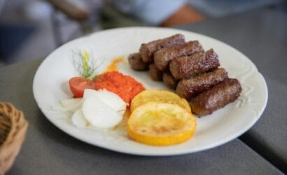 Plate of flavorful grilled cevapi with fresh vegetables and red pepper sauce. Perfect traditional Balkan meal.