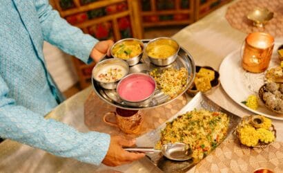 A person serving a traditional Indian thali, featuring a variety of dishes, during a festive indoor dinner setup.
